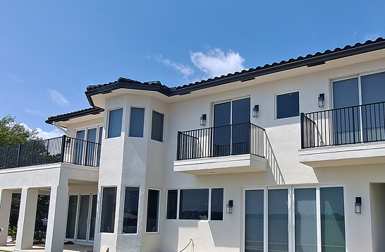 Modern two-story house with a black metal railing balcony, artificial turf yard, and a partially built pool, surrounded by palm trees and a sunny sky 2