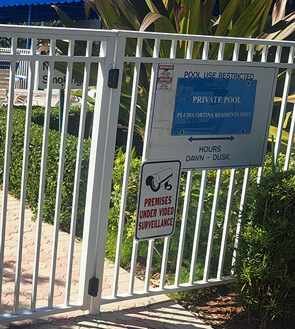White gated entrance to a private pool area with a sign indicating restricted pool use for residents only, along with a video surveillance warning sign.